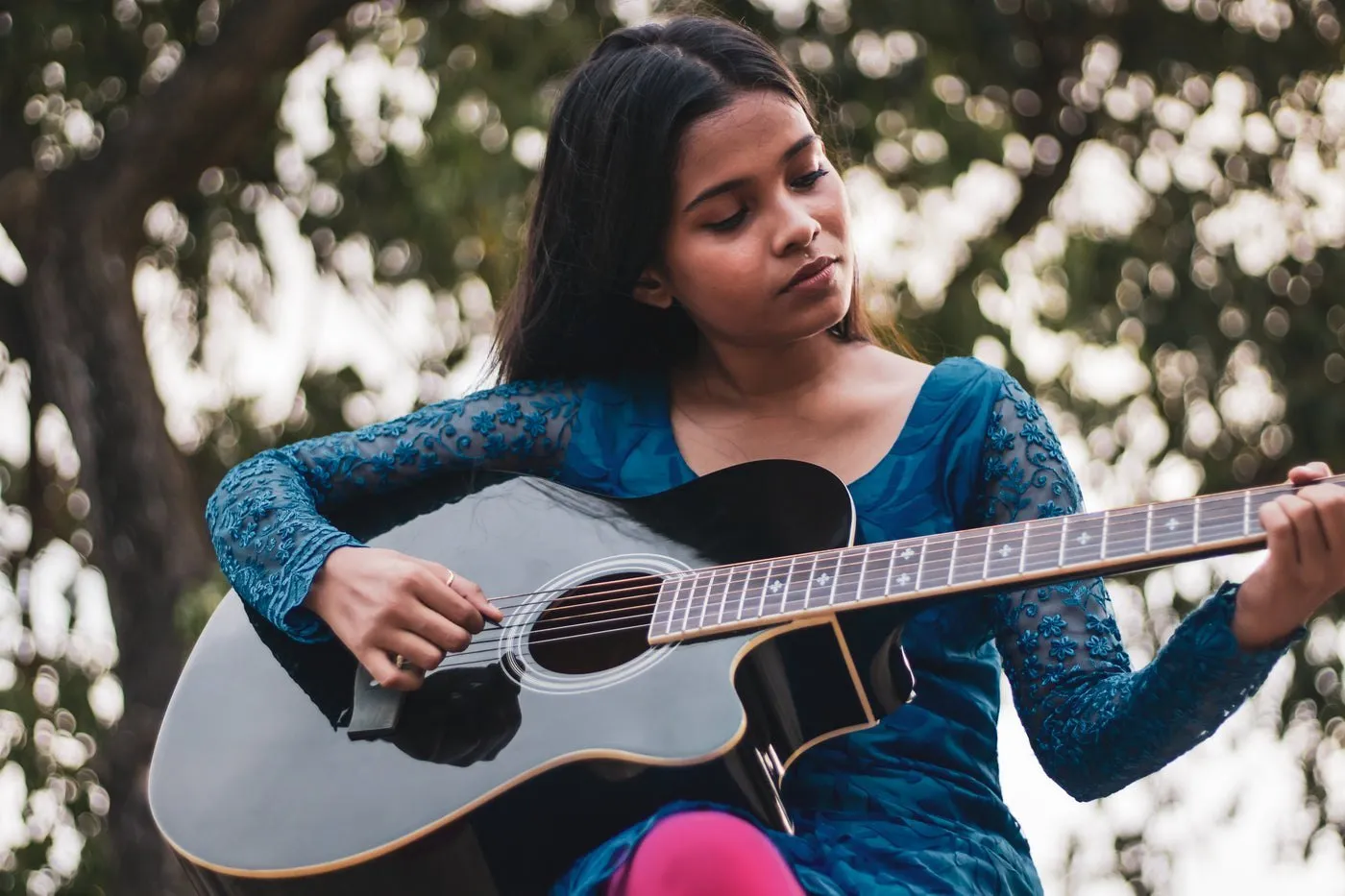 Une jeune femme joue de la guitare sous les arbres